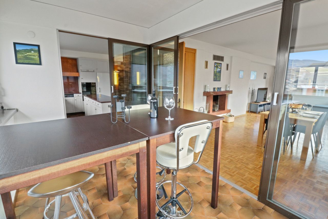 A modern kitchen with a bar area, wooden flooring, and a view through a glass door.
