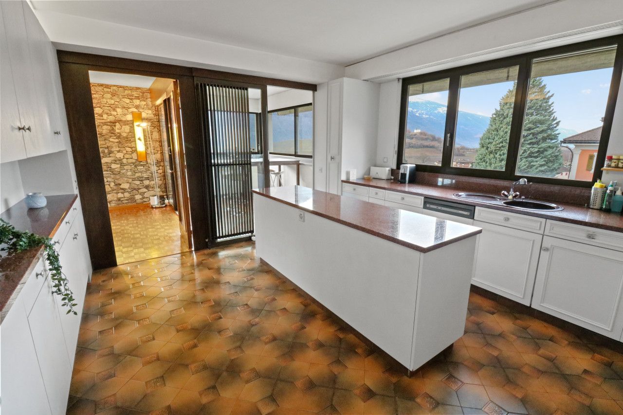A modern kitchen with a large island, white cabinetry, and a view of mountains through the windows.