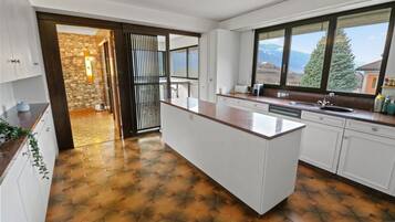 A modern kitchen with a large island, white cabinetry, and a view of mountains through the windows.