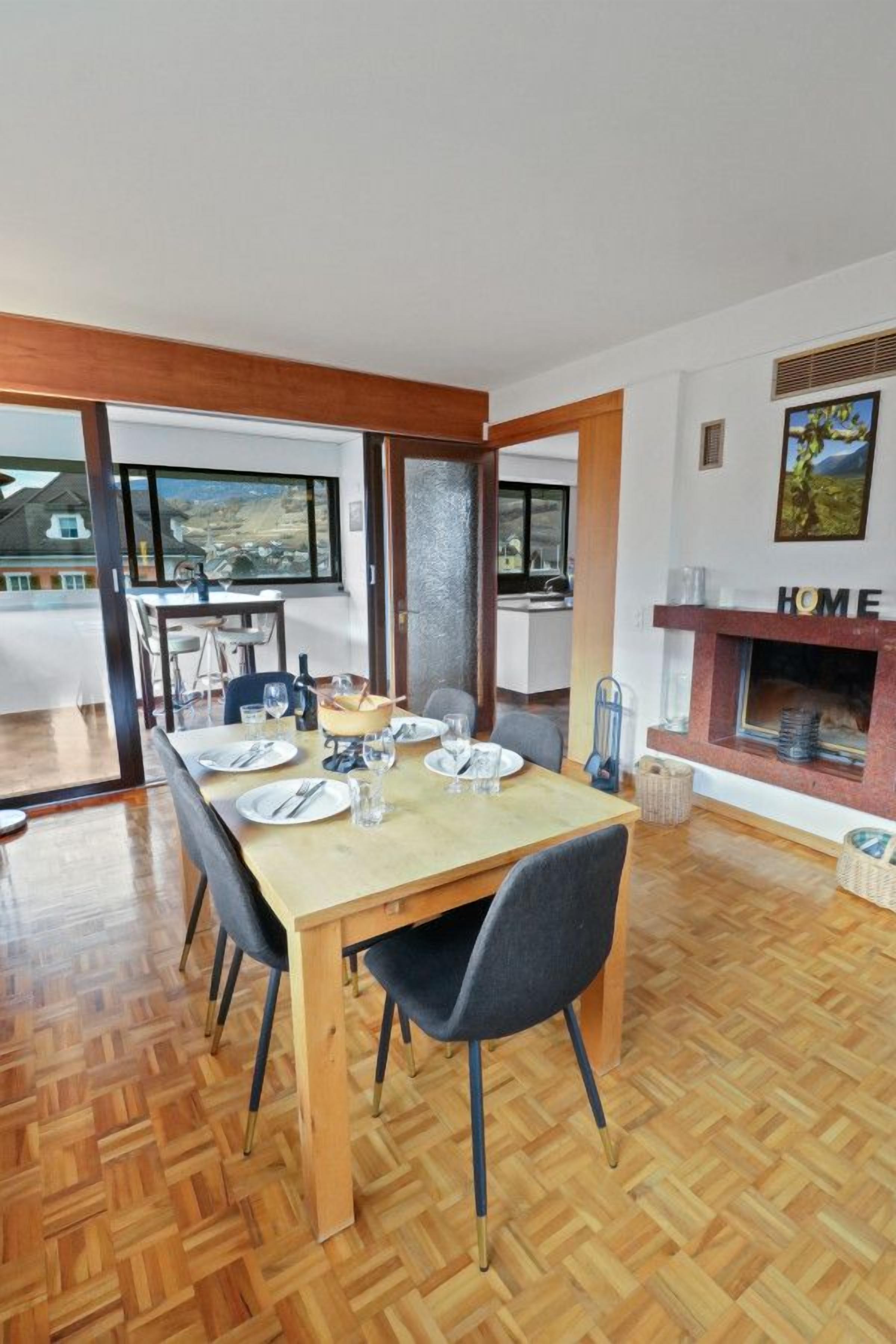Un coin repas avec une table en bois dressée pour quatre personnes, une cheminée et une vue à travers une porte vitrée.