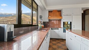 Eine Küche mit weißen Schränken, einer Arbeitsplatte aus Granit, einem eingebauten Ofen und einem Fenster mit Blick auf eine gebirgige Landschaft.