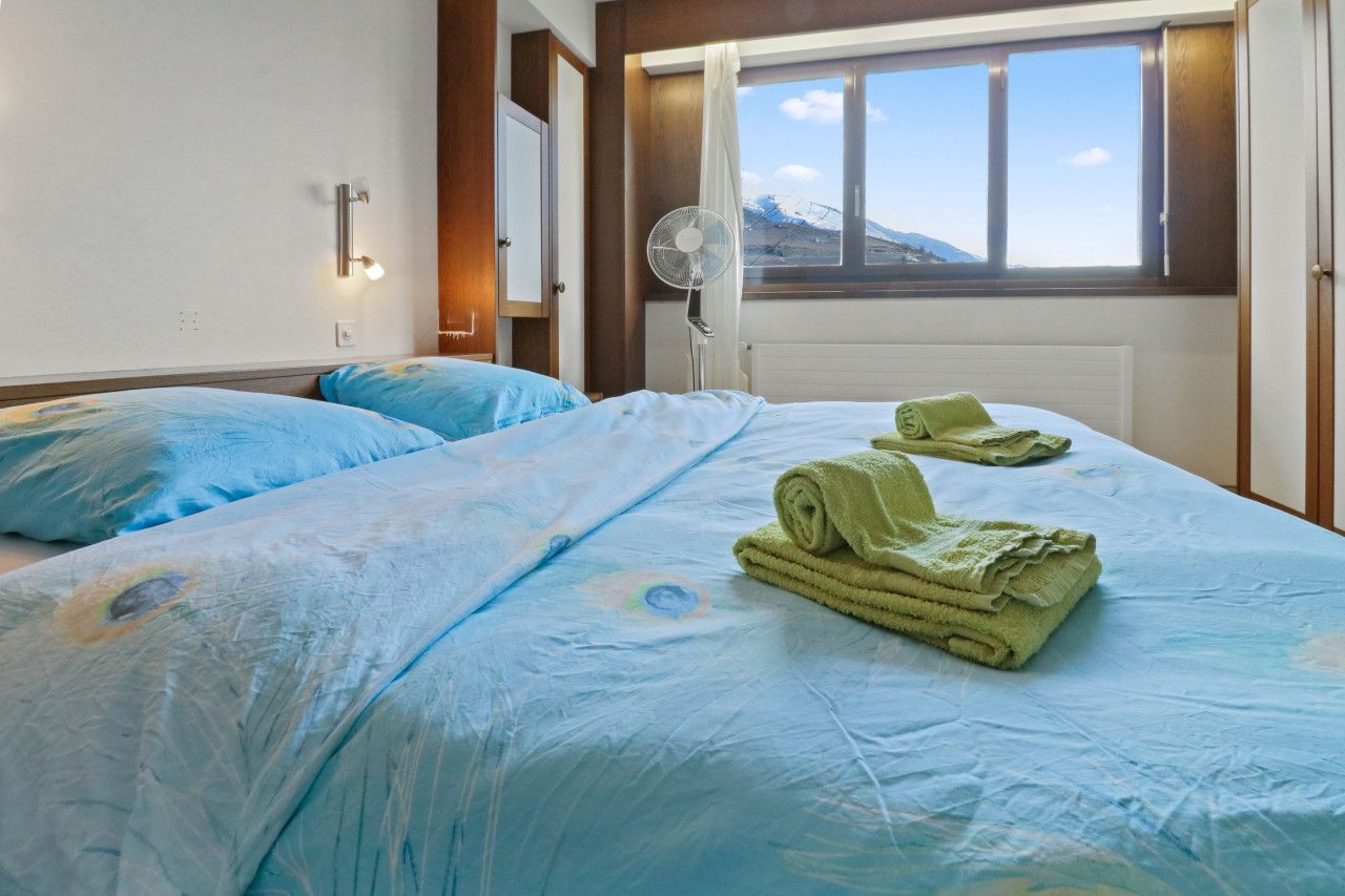 Ein Hotelzimmer mit zwei Betten, einem Fenster mit Blick auf die Berge, einem Standventilator und einer wandmontierten Lampe.