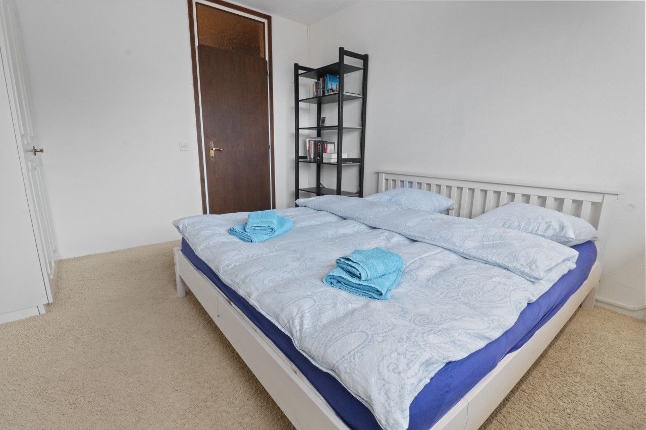 A bedroom with a white bed, a blue and white patterned bedspread, and a white radiator.