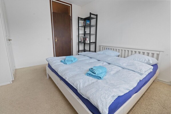 Ein Schlafzimmer mit einem weißen Bett, einer Bettdecke in Blau und Weiß sowie einem weißen Heizkörper.