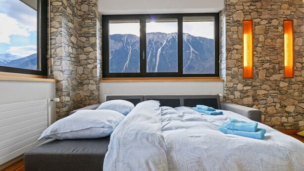 Ein Schlafzimmer mit Steinwand, einem großen Fenster mit Bergblick, einem Bett mit weißer Bettwäsche und einem Nachttisch mit Lampe.