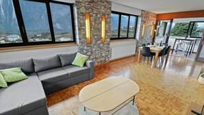 Ein modernes Wohnzimmer mit einem grauen Ecksofa, einem runden Couchtisch und einem Essbereich mit Holztisch und Stühlen.