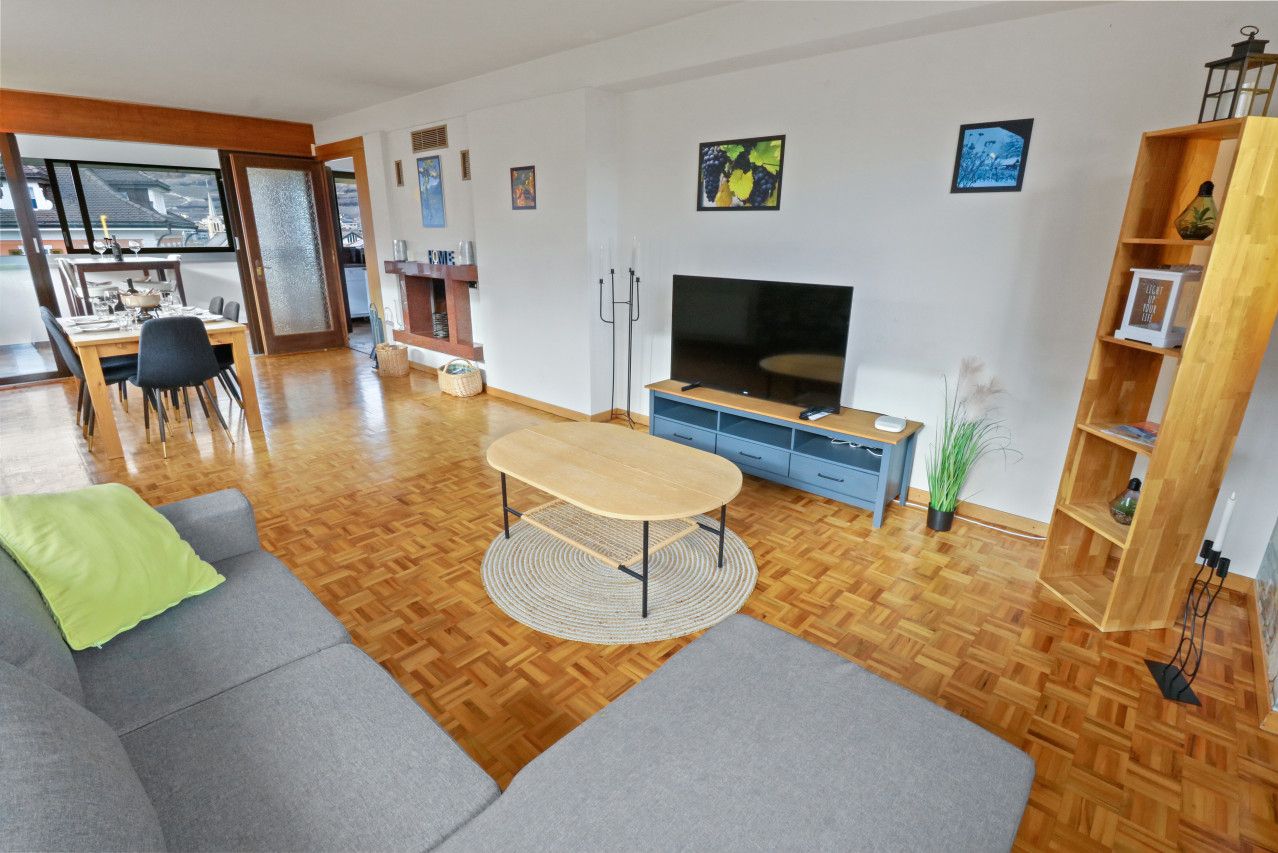 Un salon moderne avec un plancher en bois, des canapés gris, une table basse en bois, un téléviseur et une bibliothèque.