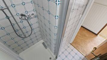 Ducha con puerta de cristal y manija de metal, paredes con azulejos de un diseño geométrico, y puerta de madera con manija de latón.