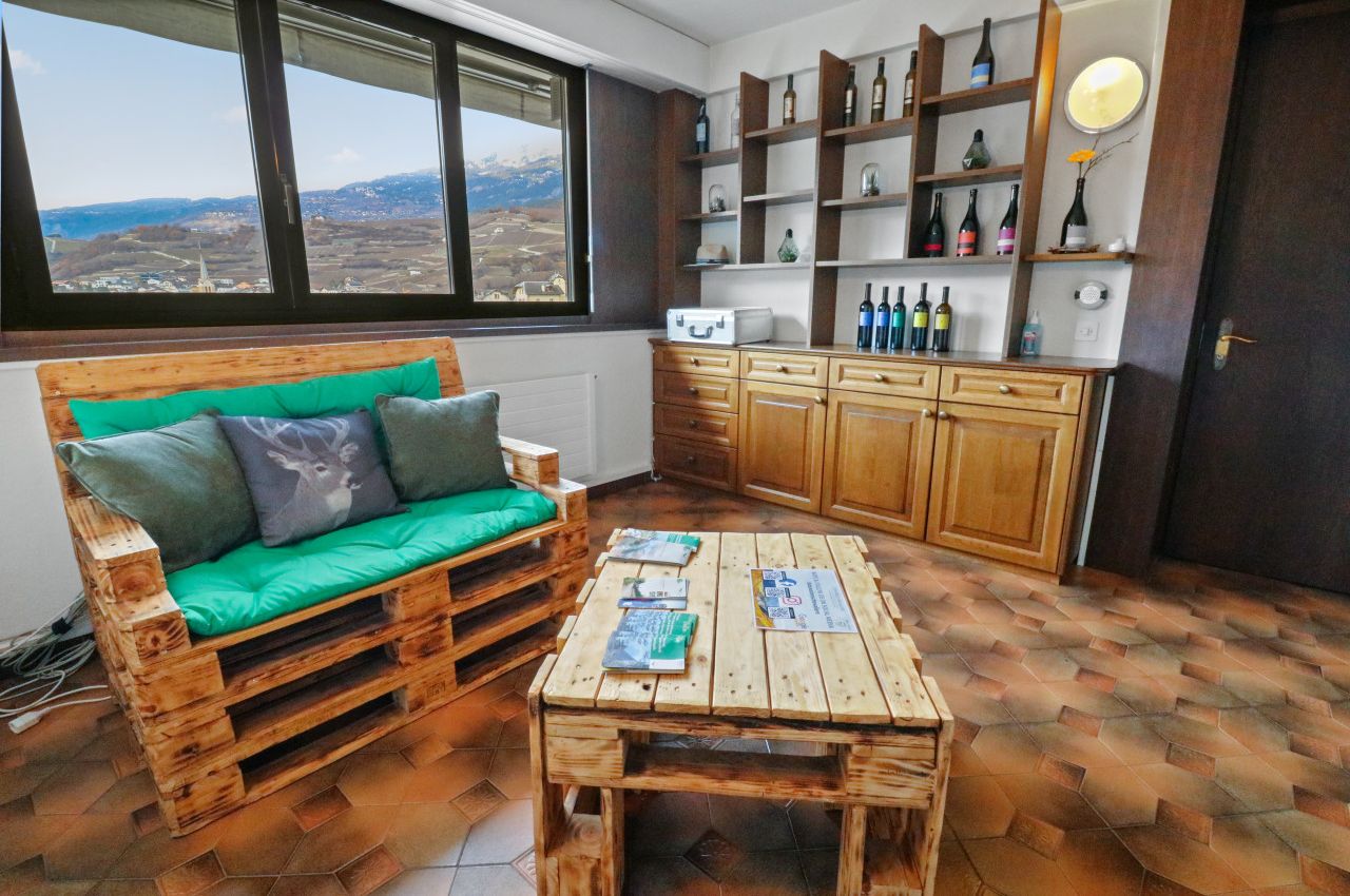 Ein gemütliches Zimmer mit einer Schlafsofa aus Holzpaletten, einem Holztisch und einem Weinregal.