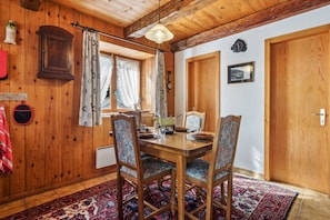 Een houten eethoek met een tafel gedekt voor vier personen, stoelen, een hanglamp en een kamerkleed met een patroon.