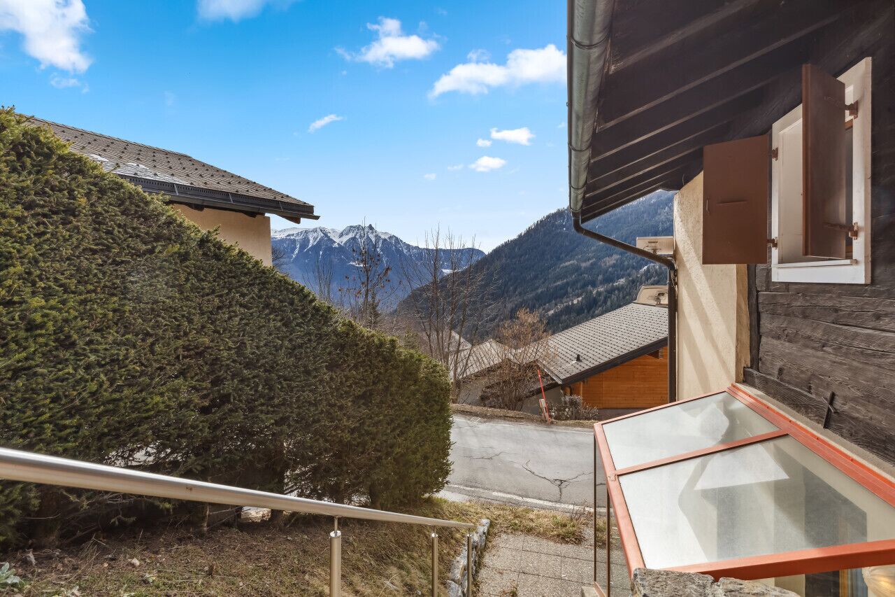 Une vue sur la montagne depuis un chalet en bois doté d’un balcon en verre donnant sur une route et une chaîne de montagnes.