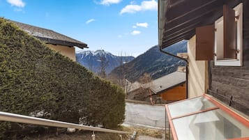 Blick auf Berge von einer Holzhütte mit einem Glasbalkon, der auf eine Straße und ein Bergmassiv blickt.