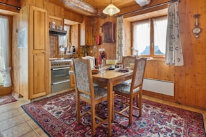 A wooden interior with a dining table, chairs, and a patterned rug.