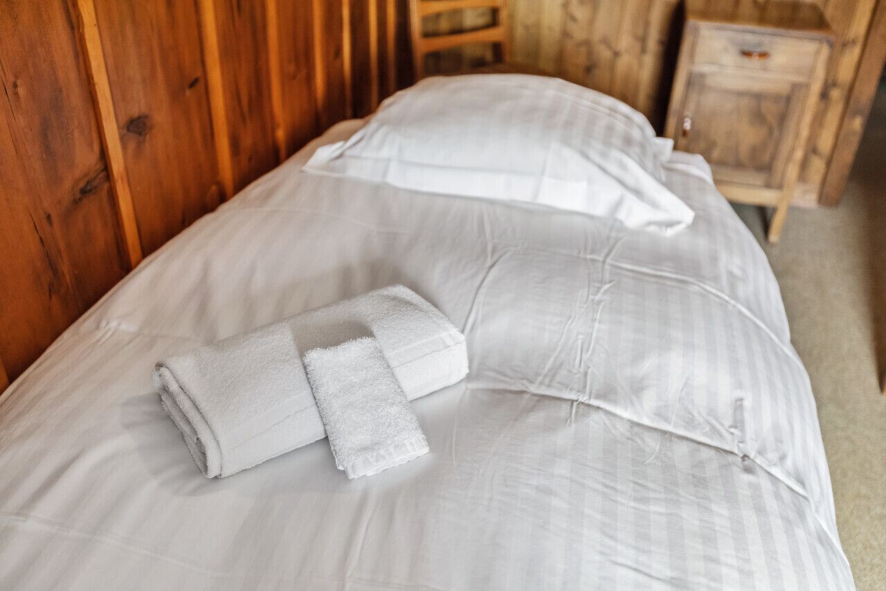 Een bed met witte lakens en twee opgerolde handdoeken.
