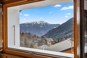 Uitzicht vanuit een raam op een berglandschap met een huis en een bergketen.