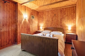 A wooden-paneled bedroom with a bed, two bedside tables, and wall-mounted lamps.
