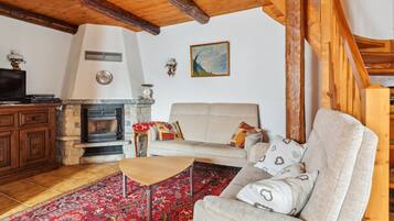 Ein Wohnzimmer mit Kamin aus Stein, einer Couch, einem Couchtisch und einem Teppich mit Muster.