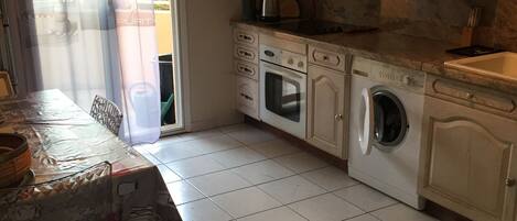 A kitchen with white cabinets, a built-in oven, a washing machine, and a dining table with a covered chair.