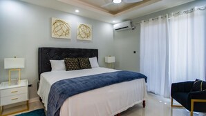 Une chambre à coucher moderne avec un grand lit, des tables de chevet, une chaise et des œuvres d’art accrochées au mur.