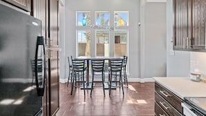A kitchen with a dining table and chairs, wooden cabinets, and a refrigerator. - Retreat Port Aransas | A Retreat DFW Experience (Port Aransas)