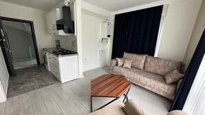 A modern living room with a sofa, a coffee table, and a kitchen area with a stove and cabinets. - Trabzon White Life (Trabzon)
