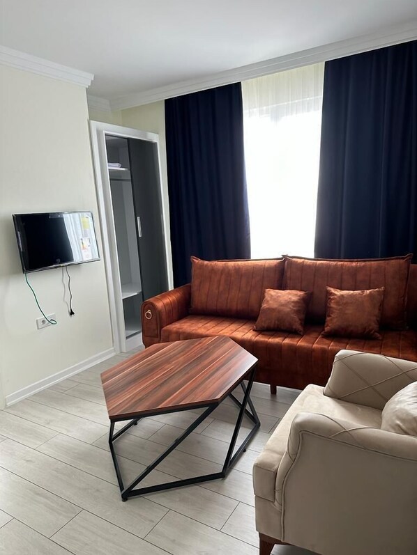 A living room with a brown leather sofa, a wooden coffee table, and a beige armchair. A flat-screen TV is mounted on the wall. - Trabzon White Life (Trabzon)