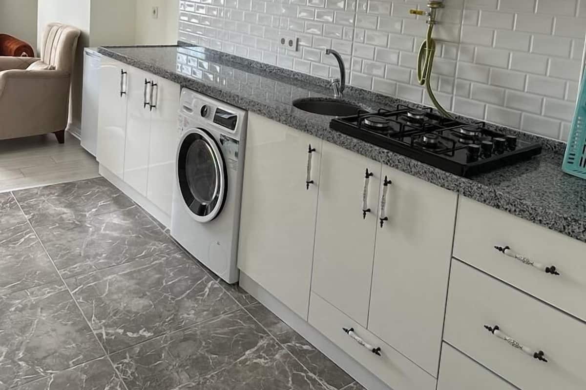 A modern kitchen with white cabinets, a built-in washing machine, a gas stove, and a black range hood.
