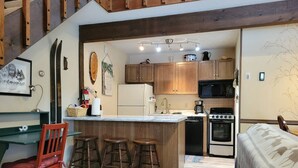 Una cocina compacta con armarios de madera, una isla central con taburetes, microondas, horno y refrigerador.