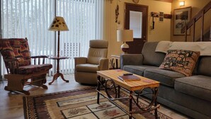Una sala de estar acogedora con techo de madera, un sofá, un sillón mecedora, una mesa y una lámpara.