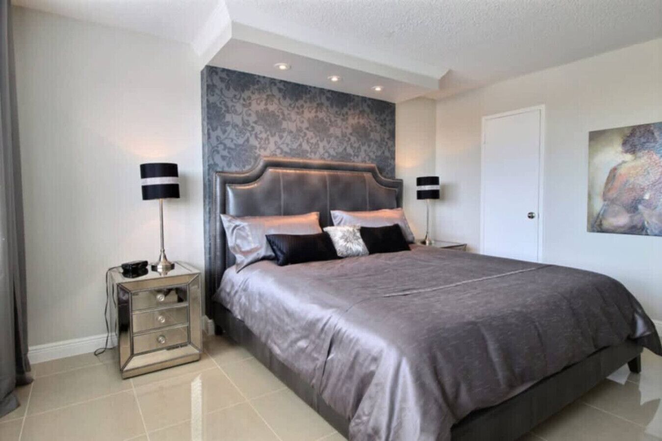 Een moderne slaapkamer met een groot bed, twee nachtkastjes, een decoratieve wand en een deur.