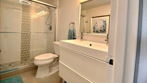 A modern bathroom with a glass shower enclosure, a toilet, a sink with a mirror, and a towel rack. - golden isles # 509 Water view (Hallandale Beach)