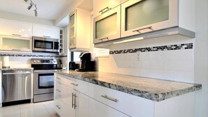 A modern kitchen with stainless steel appliances, white cabinetry, and a marble countertop. - golden isles # 509 Water view (Hallandale Beach)