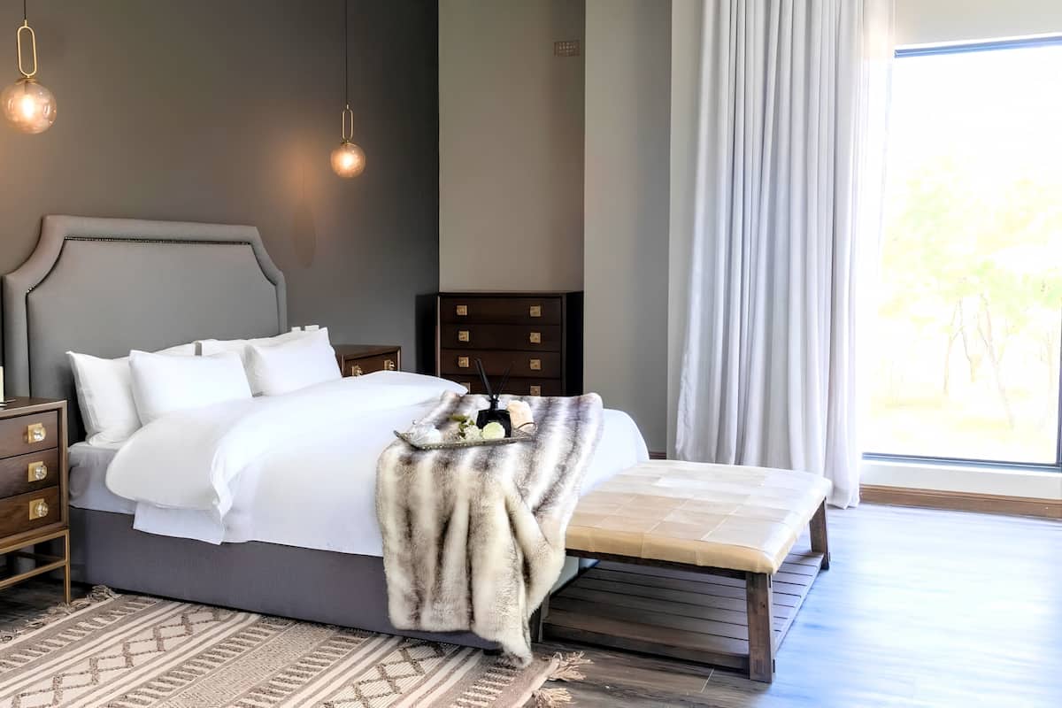 A modern bedroom with a large bed, bedside tables, a bench, and a view of the outdoors.
