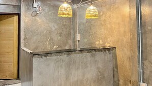 Huone, jossa on betonisesta materiaalista valmistettu vastaanottotiski, näkyviin jätetyt kattoputket ja kaksi riippuvalaisinta.