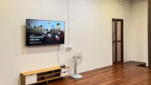 Huoneessa on puulattia, seinälle asennettu televisio, valkoinen tuuletin ja puinen penkki.