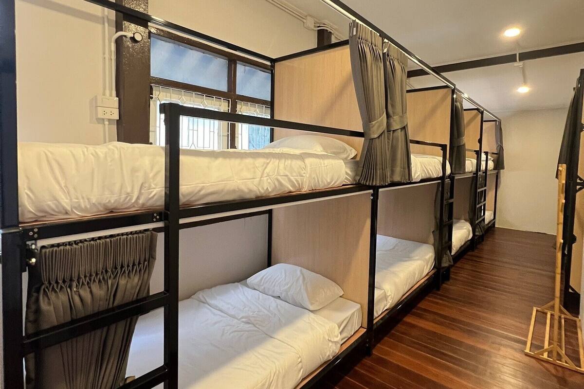 A bunk bed room with wooden flooring, a window with curtains, and a ceiling light.
