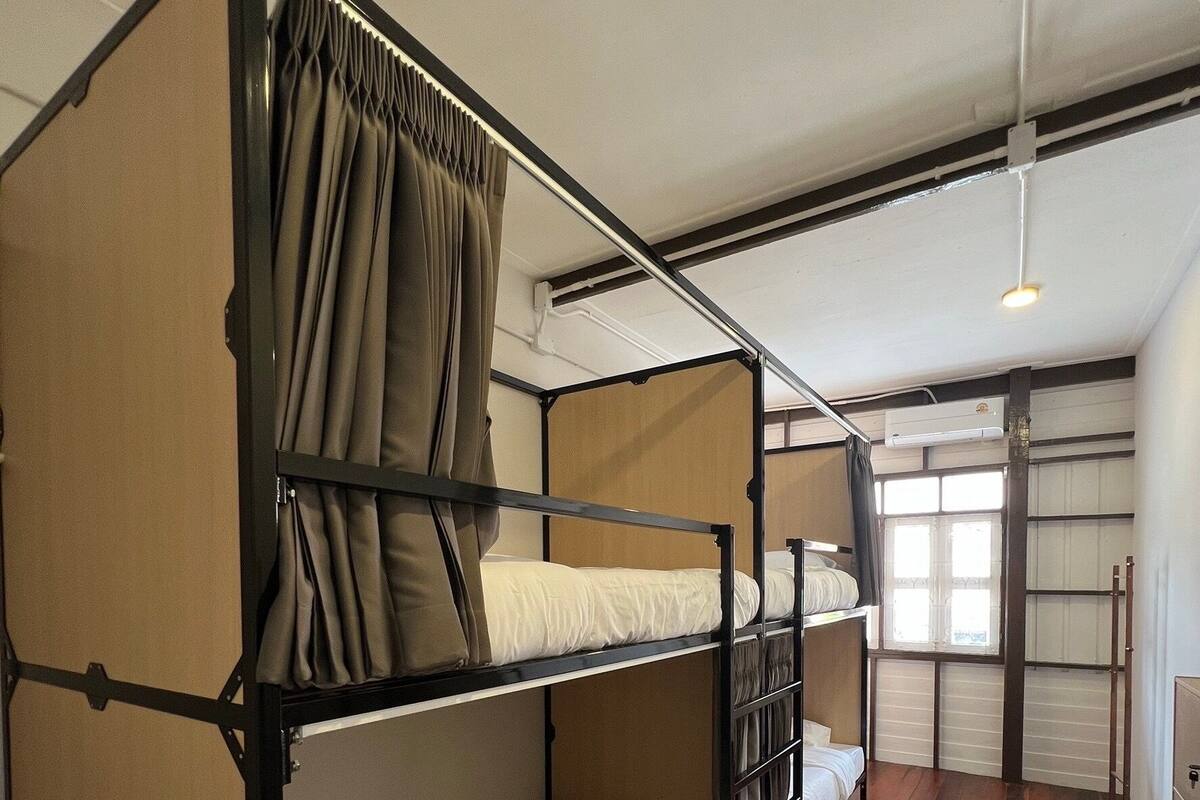 A bunk bed room with a wooden floor, a window with curtains, and an air conditioning unit on the wall.