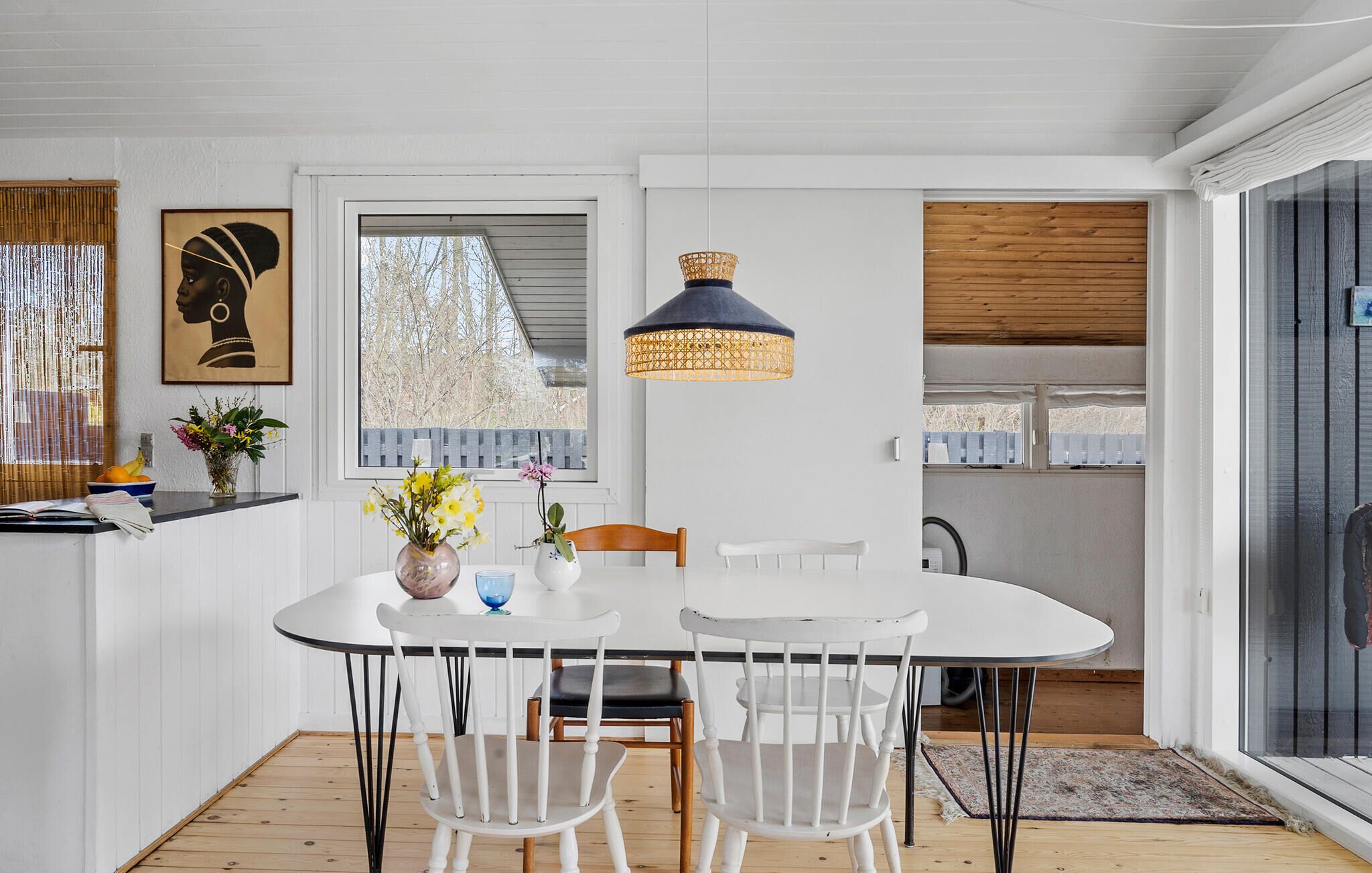 Spiseplads med et hvidt bord, to hvide stole, en vase med blomster og en hængende lampe.