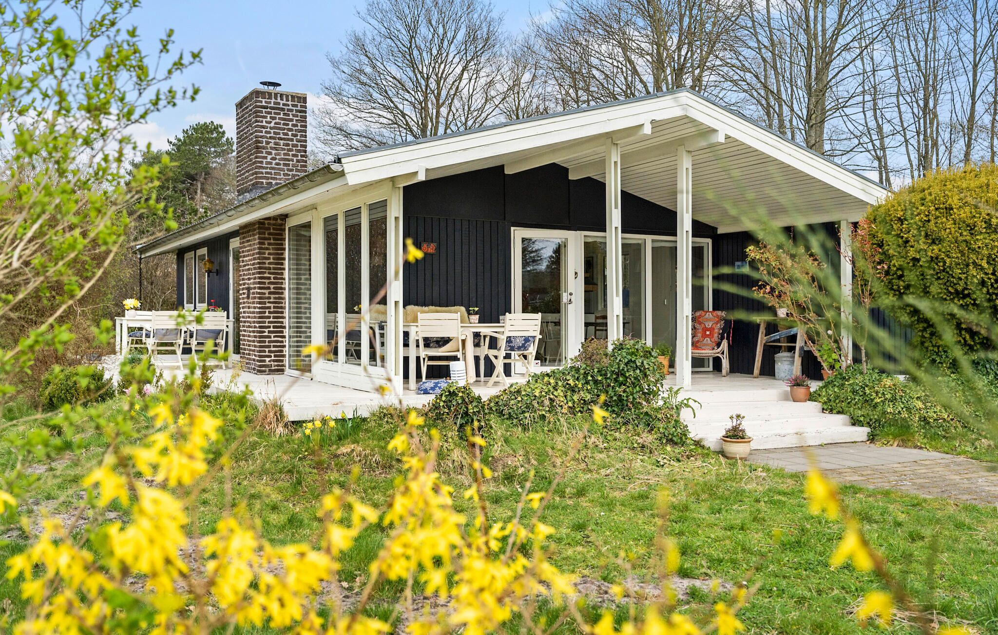 A house with a covered porch, a brick chimney, and a garden with yellow flowers.