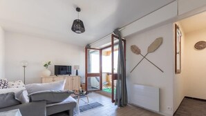 A modern living room with a grey sofa, a TV, and a wooden cabinet. - Studio Les Vacances a Andernos (Andernos-les-Bains)