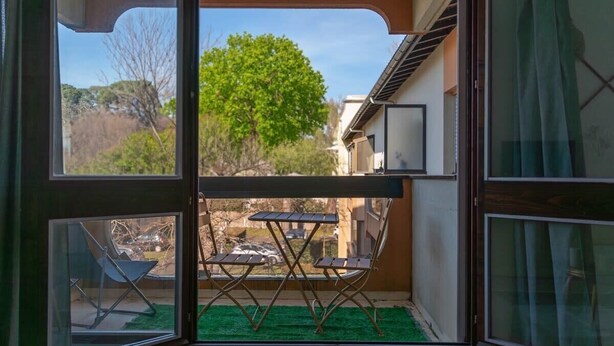 A balcony with a table and chairs, a view of a tree, and a building in the background. - Studio Les Vacances a Andernos (Andernos-les-Bains)