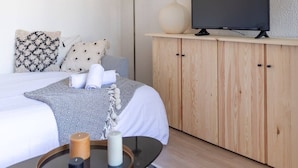 A modern hotel room with a bed, a TV on a wooden cabinet, a floor lamp, and a small table with candles. - Studio Les Vacances a Andernos (Andernos-les-Bains)