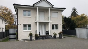 Ein zweistöckiges Haus mit einer symmetrischen Fassade, einem zentralen Eingang mit Treppe und einem überdachten Veranda.