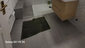 A modern bathroom with a herringbone tile backsplash, a shower with a glass door, a vanity with a mirror, and a radiator. - Ajaccio Cosy & Charm (Ajaccio)