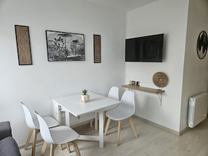 Un espace repas moderne avec une table blanche, quatre chaises blanches, une petite plante en pot et des œuvres d’art accrochées au mur.