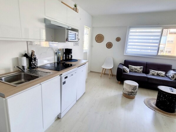 A compact living space with a kitchenette, a sofa, and a dining area. - Apartment 500m from the sea, 4 sleeps, secure parking (Courseulles-sur-Mer)
