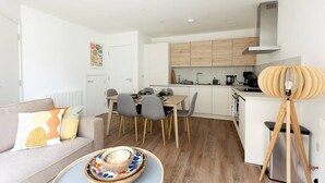 Una cocina moderna con armarios de madera, un comedor con mesa y sillas, un sofá con cojines estampados y una lámpara de pie original.