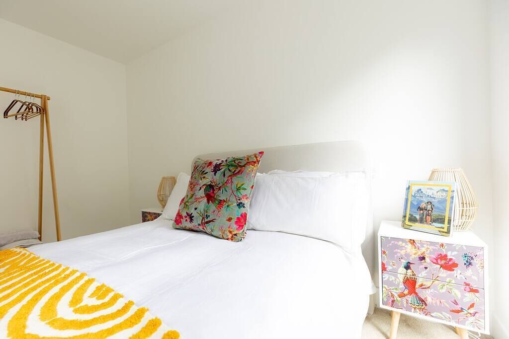 A neatly made bed with a floral pillow, a bedside table with a decorative item, and a hanging rack.