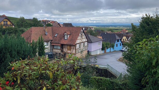 Un village européen traditionnel, avec des maisons à colombages, une rue pavée et une vue sur la campagne environnante.