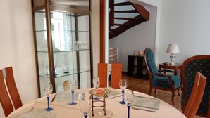 Zona de dinar amb una taula rodona preparada per a sis, un vitrina amb vidres de vi, una escala de fusta i una cadira tapissada de blau.